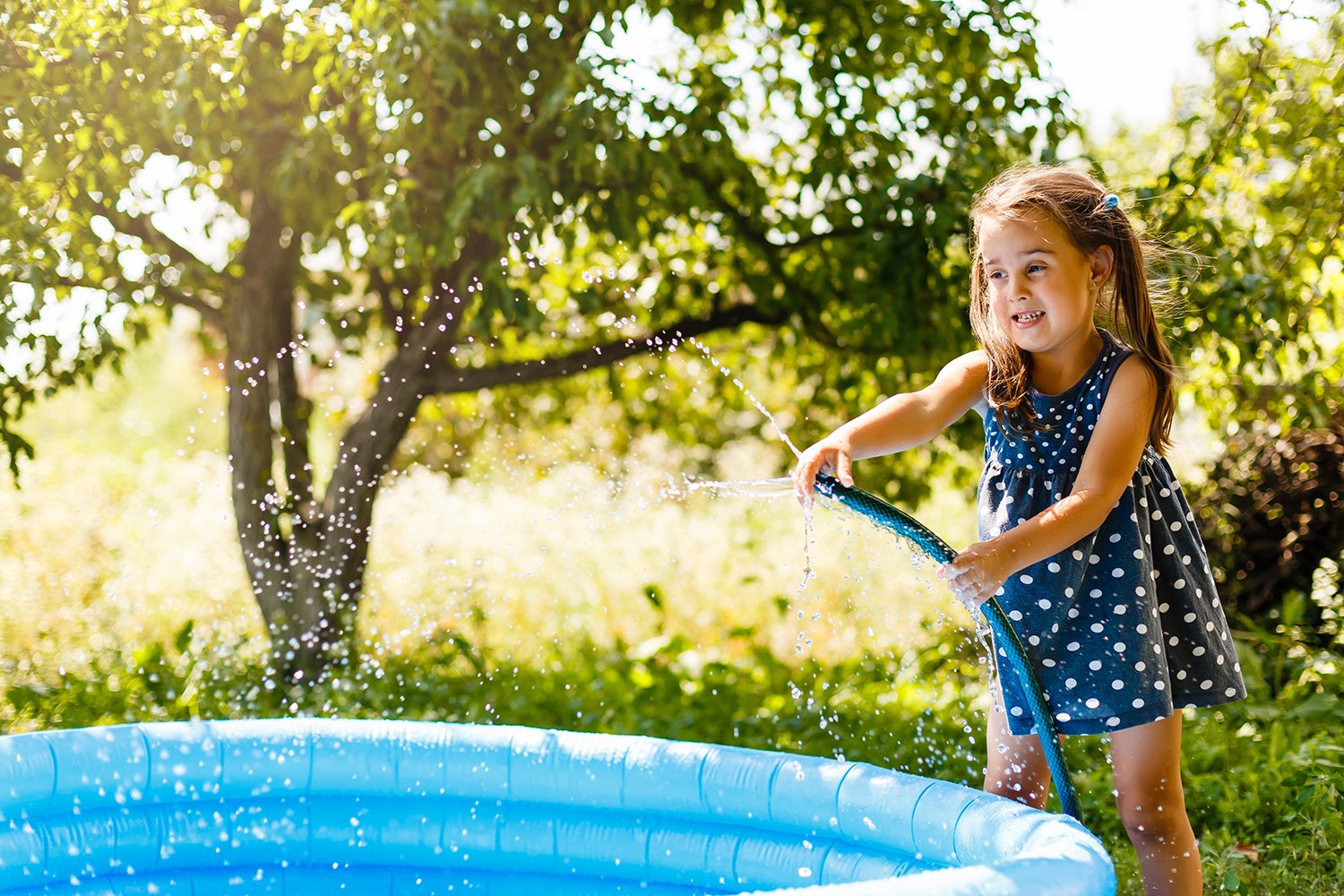 En flicka med två tofsar som fyller en pool med vatten. 