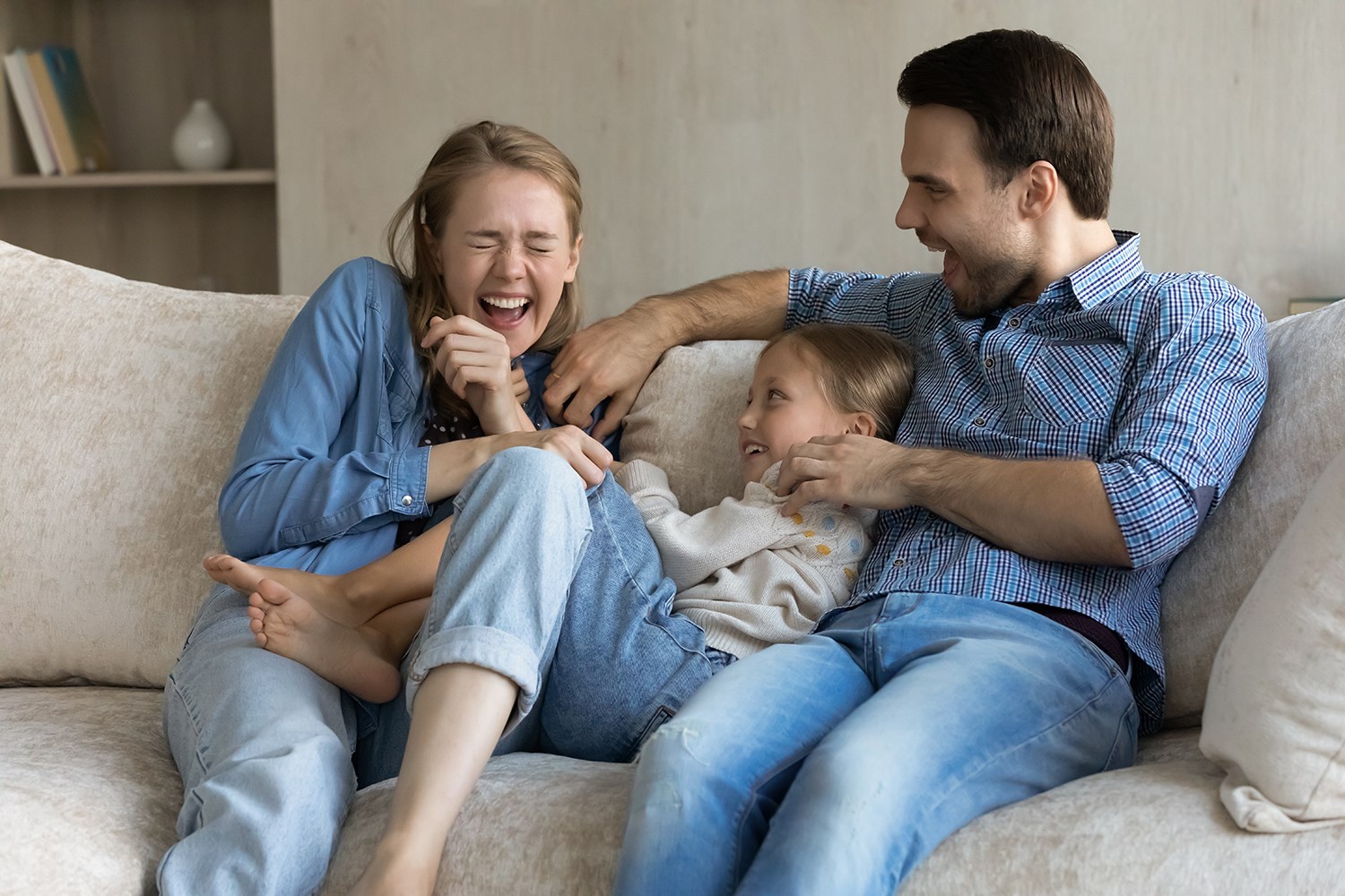 Mamma, pappa och barn i soffa som skrattar och kittlas. 