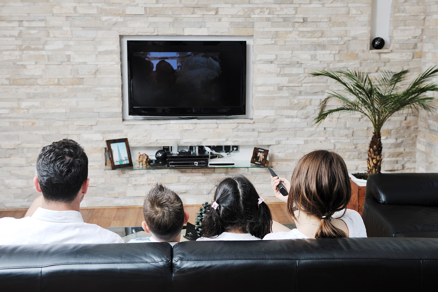 En familj om fyra personer, sitter i soffan och tittar på TV.